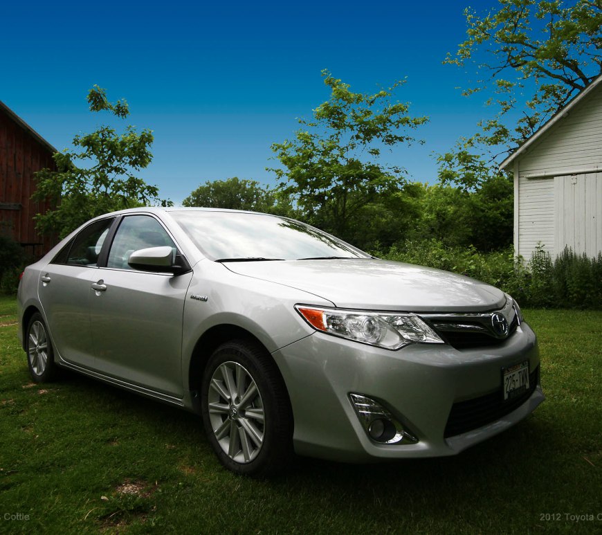 Silver Toyota Camry Hybrid framed by barns in the background