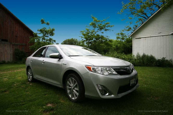 Silver Toyota Camry Hybrid framed by barns in the background