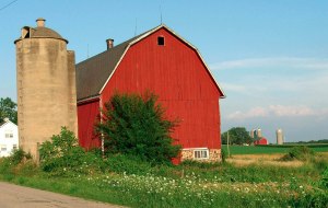 A traditional red barn with a stone foundation in the foreground with similar structures in the background a half mile away.