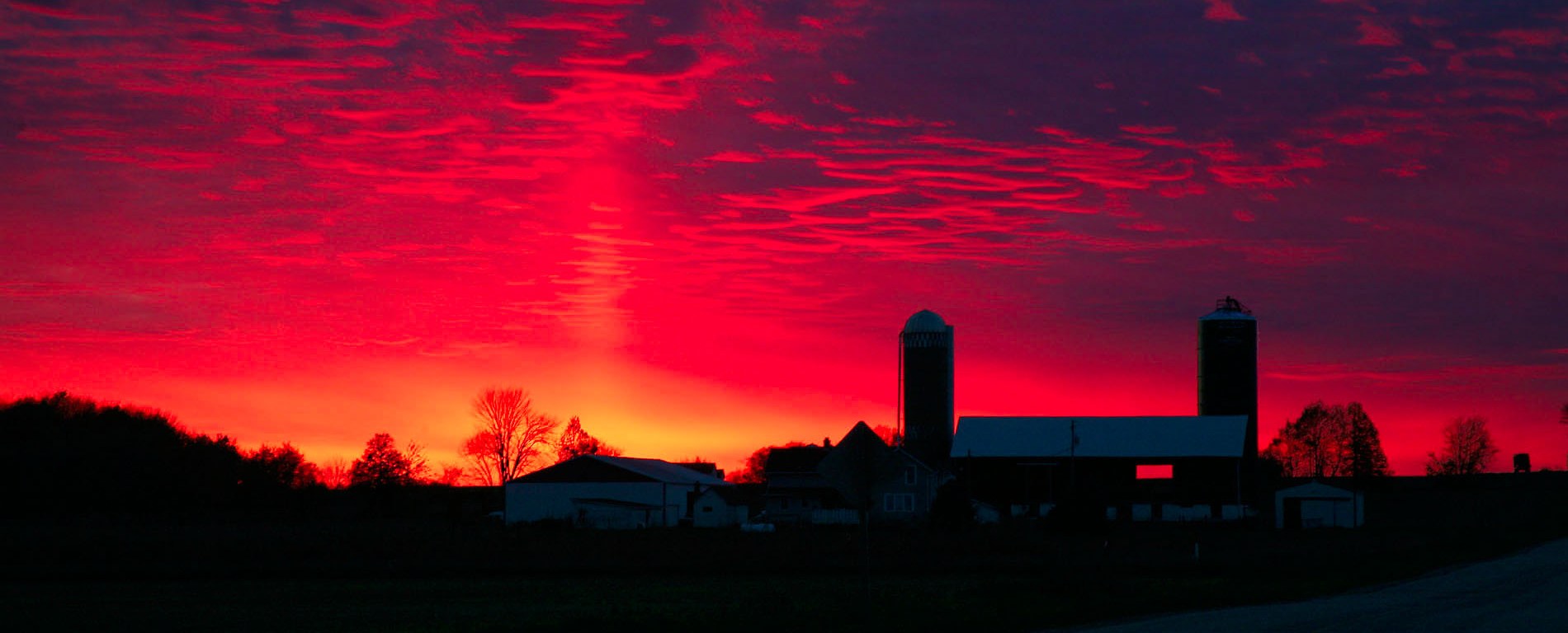 Vibrant red sunset with farm buildings in silhouette