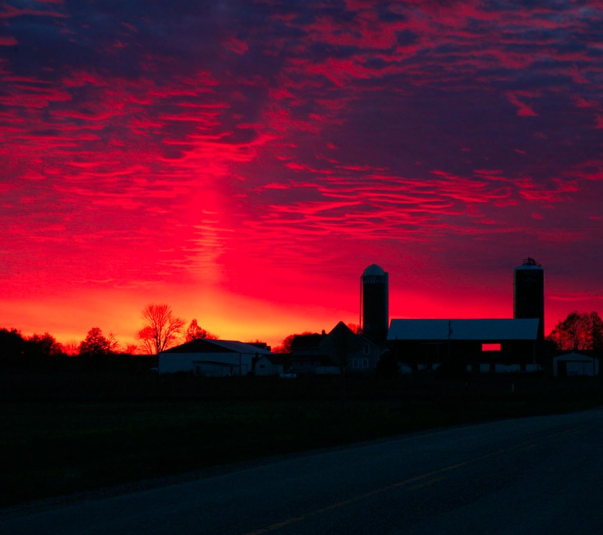 Vibrant red sunset with farm buildings in silhouette
