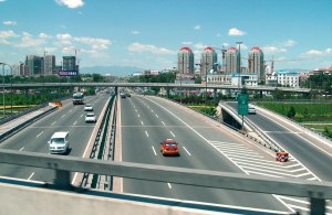 Contemporary highway scene with six lanes of traffic, multiple overpasses, and high buildings in the distance